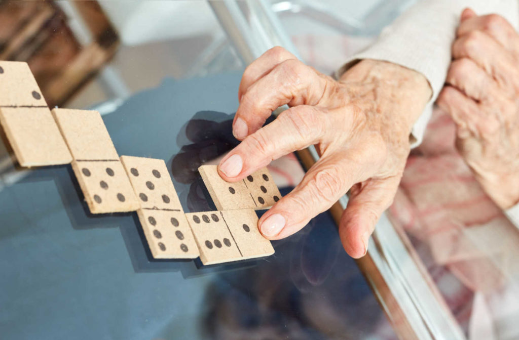 A senior's hand places a domino onto the table next to another one.
