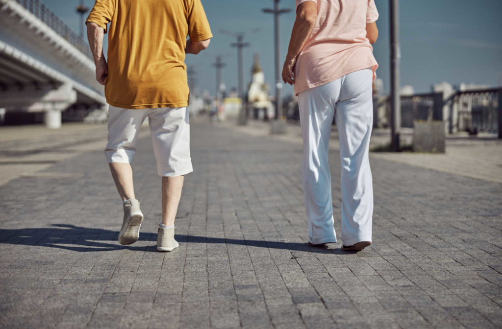 Cropped image of an elderly man in shorts and his wife in trousers walking outdoors.