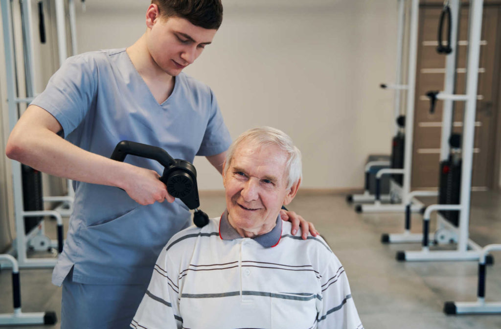 A caregiver giving a massage to a senior man using a using a massage gun.