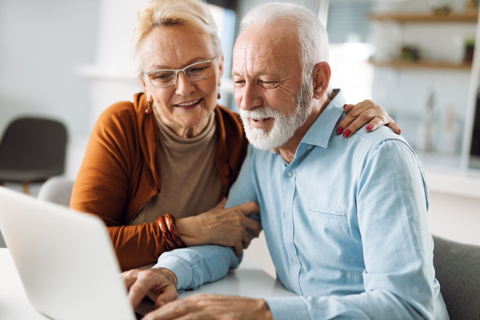 A senior couple smiling together in their home while researching independent living communities.