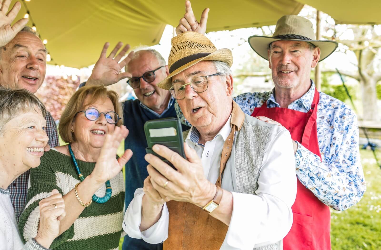 A group of new senior friends gather together outside as one gets a video call