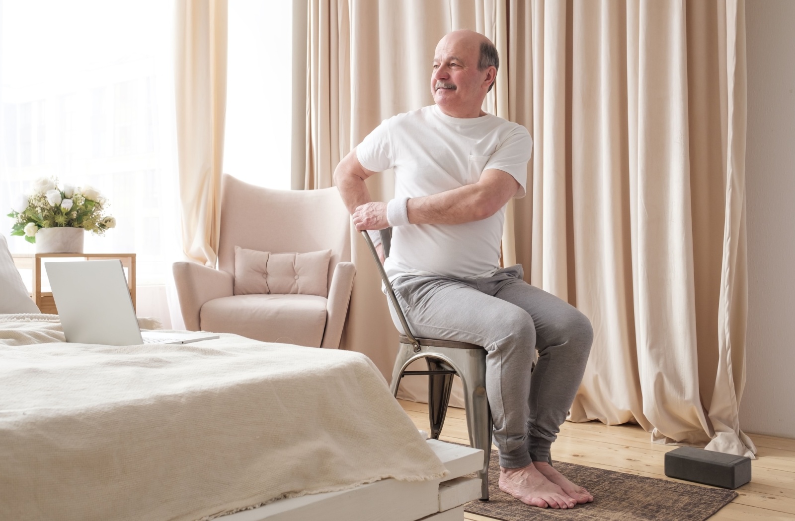 Older man performing a seated stretch, improving posture, in a bright room with natural light.