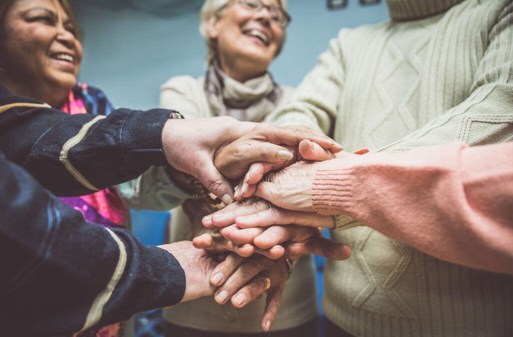A group of seniors stack their hands on top of each other as an icebreaking activity at a community event.