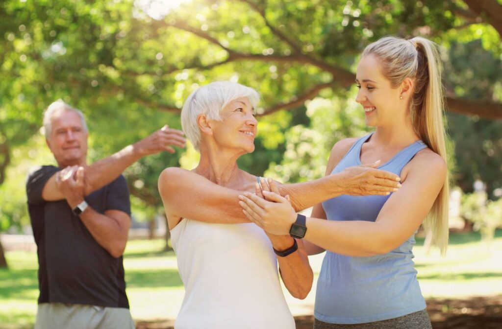 A fitness instructor helps a senior get the right stretch for cooling down after their outdoor fitness class
