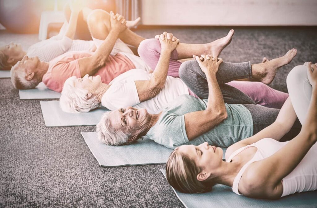 A group of seniors holds their knees to their chests while lying on mats during a yoga class in senior living