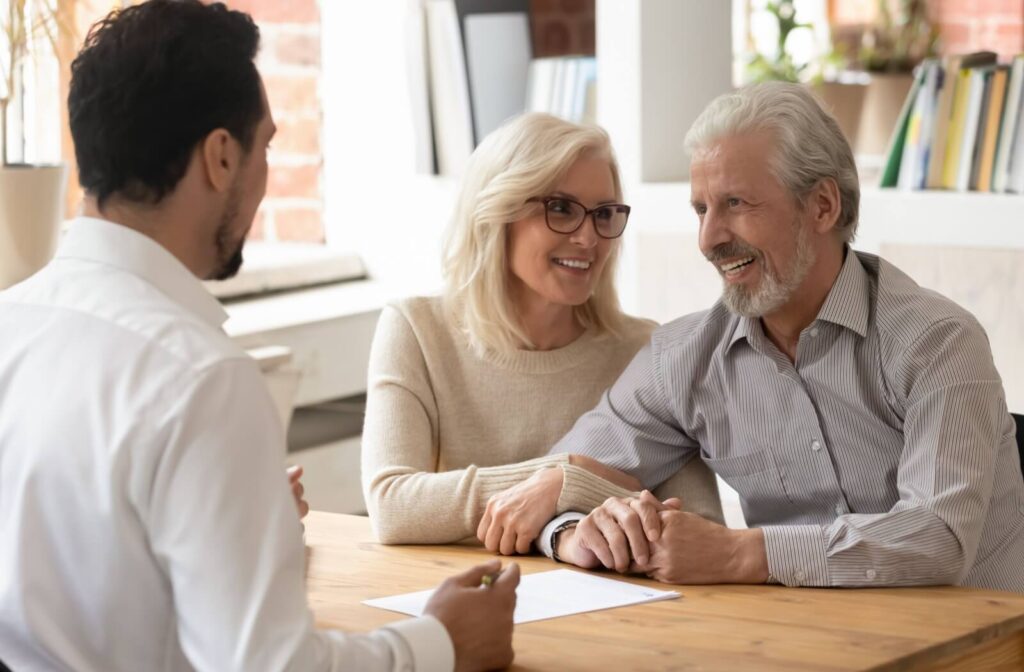 An older adult looks at their spouse, grabs their arm, and smiles during an application with a representative of an independent living community