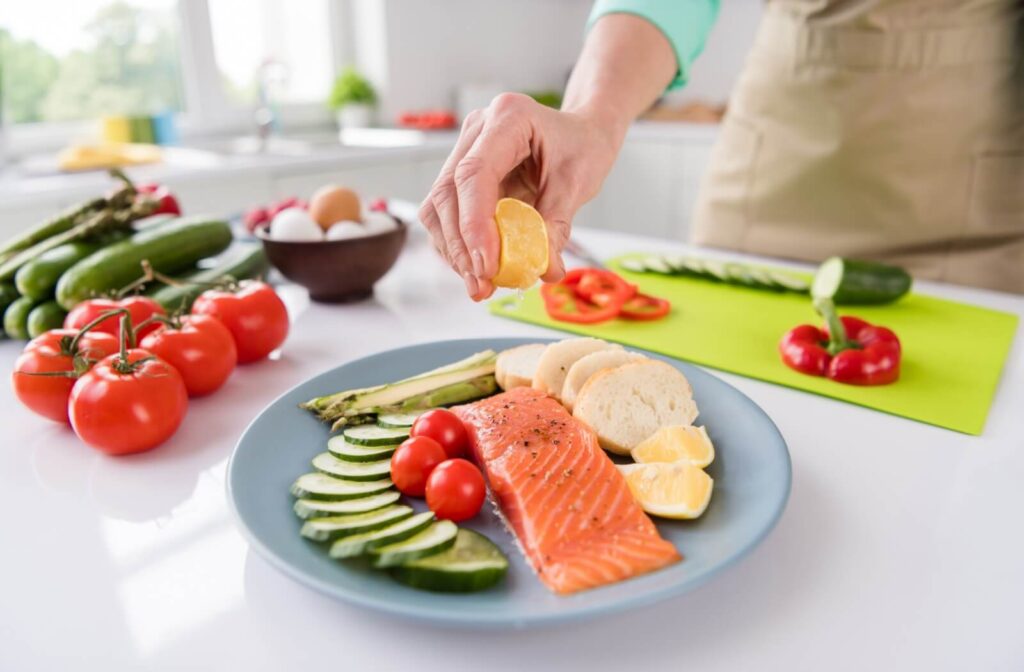 A senior squeezes a lemon onto a freshly cooked salmon plated with vegetables that benefit brain health for dinner